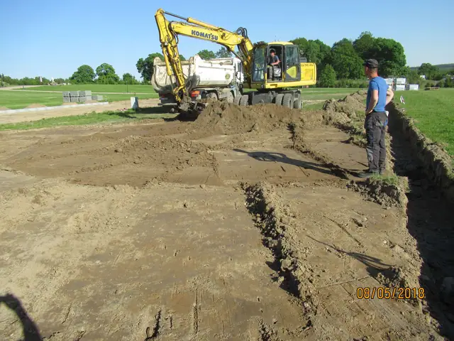 Koparka kołowa Komatsu wyrównuje pas ziemi obok trawnika przy przyszłym placu utwardzonym
