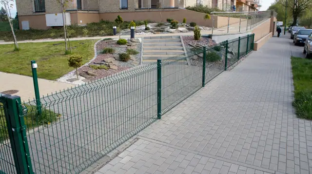 Wybrukowany chodnik i ogrodzenie panelowe wzdłuż skarpy ze skalniakiem na Osiedlu Słonecznym