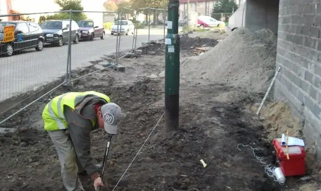 Geodeta wytycza punkty pomiarowe na wykopanym terenie przy budynku Osiedla Słonecznego