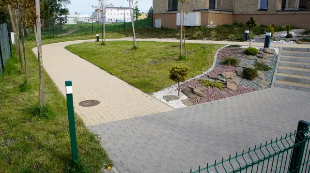 Kręta ścieżka z kostki brukowej prowadząca przez skwer z oświetleniem i skalniakiem