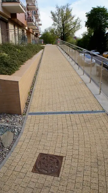 Wybrukowana pochylnia z balustradą i odwodnieniem liniowym wzdłuż zabudowań osiedla
