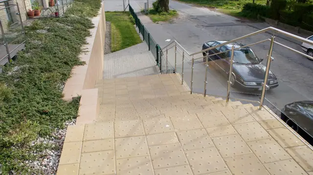 Schody z płyt chodnikowych z metalową balustradą prowadzące na ulicę przy zaparkowanym samochodzie