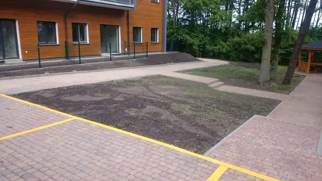 Wybrukowany dziedziniec z pasem trawnika pomiędzy drewnianymi budynkami osiedla