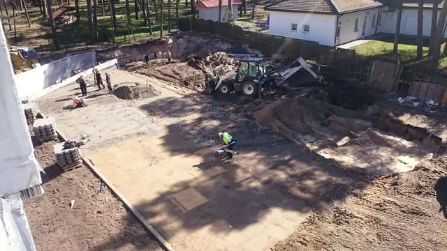 Widok z góry na małą koparkę pracującą na ogrodzonym podwórku przy domu