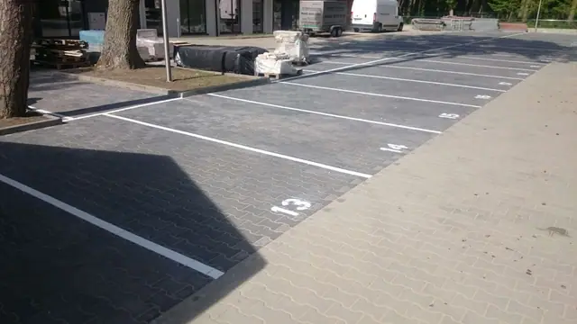 Ukończony ciemny parking z ponumerowanymi miejscami i białymi liniami wyznaczającymi stanowiska