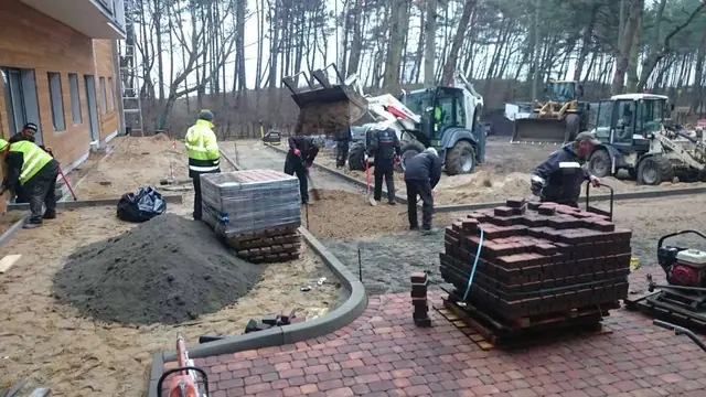 Ekipa rozładowuje palety kostki brukowej przy drewnianym budynku w Ustroniu Morskim