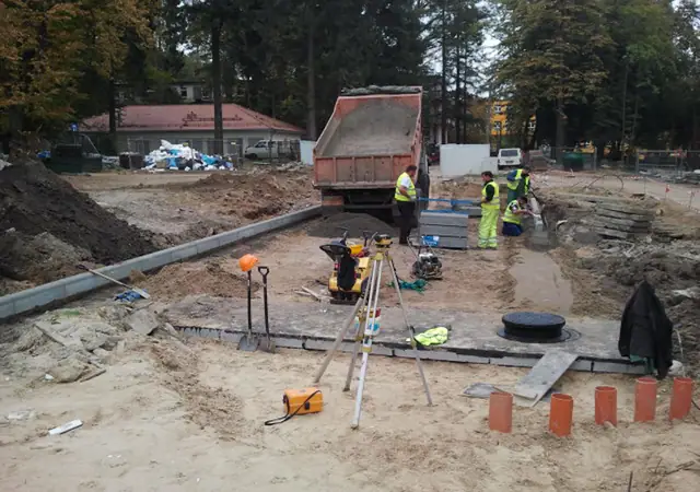 Geodeta wykonuje pomiary niwelatorem przy studzience kanalizacyjnej na terenie Szpitala Wojewódzkiego w Koszalinie
