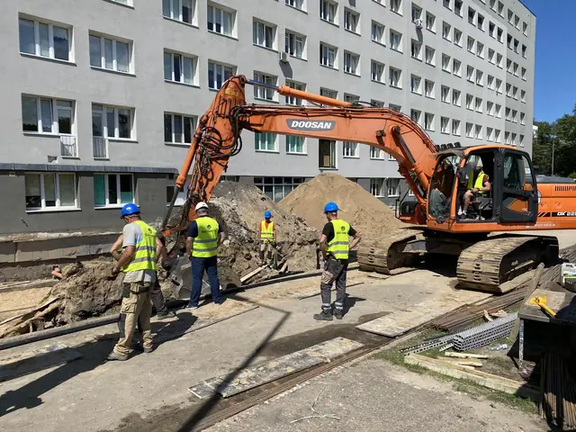 Koparka Doosan i ekipa pracują przy kopcu ziemi obok budynku szpitala