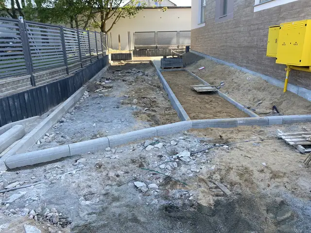 Teren z gruzem i rozbitym betonem przy elewacji budynku, żółta skrzynka elektryczna w tle
