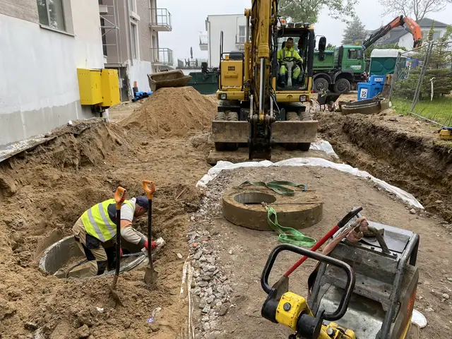 Koparka i zagęszczarka przy betonowych kręgach studziennych w głębokim wykopie