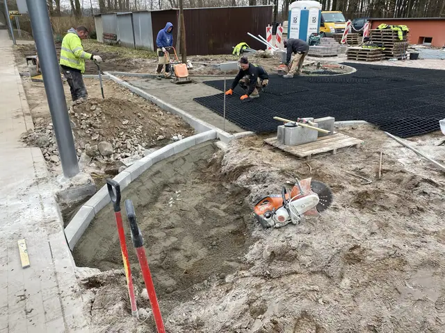 Robotnicy układają czarną kratę trawnikową i betonowe elementy przy łukowym krawężniku