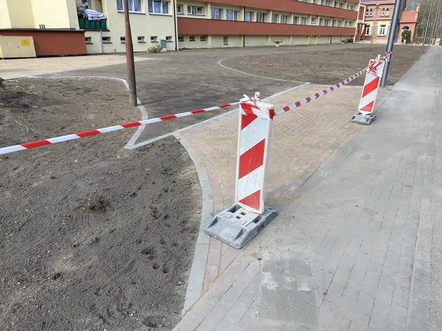 Fragment nowej nawierzchni z kostki brukowej wygrodzony taśmą ostrzegawczą na placu