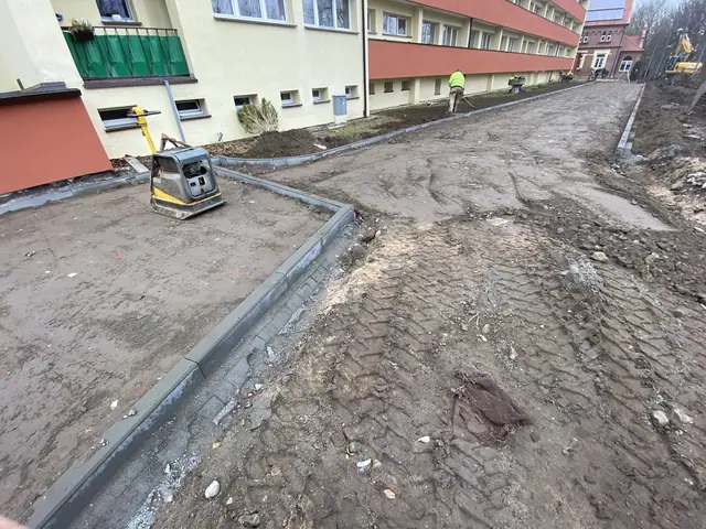 Zagęszczarka gruntu pracuje przy chodniku z kostki obok budynku DPS