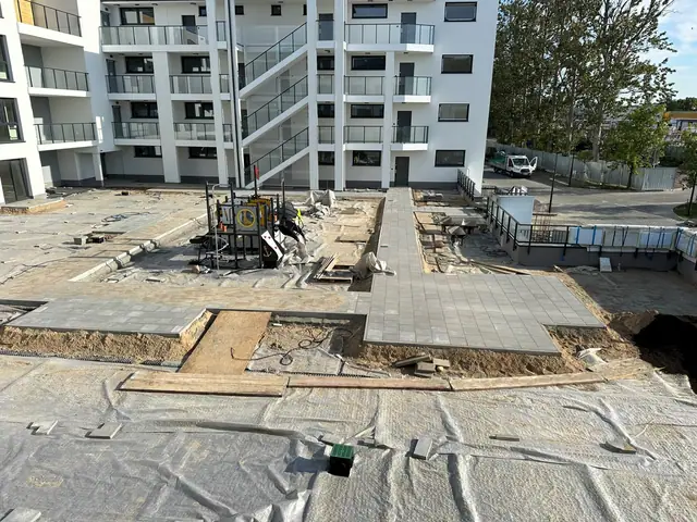 Widok z góry na plac z ułożoną kostką, placem zabaw i rozłożoną agrowłókniną wokół