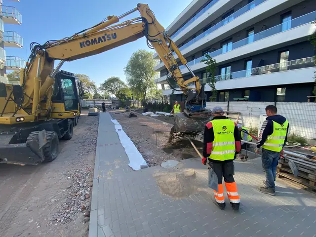 Koparka Komatsu i pracownicy Szymeta układają geowłókninę pod chodnik na osiedlu Przy Porcie