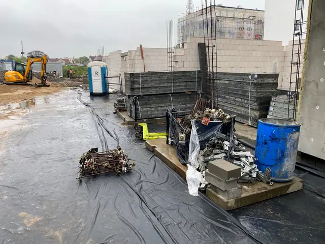 Materiały budowlane i odpady ułożone na czarnej folii przy konstrukcji nowego budynku