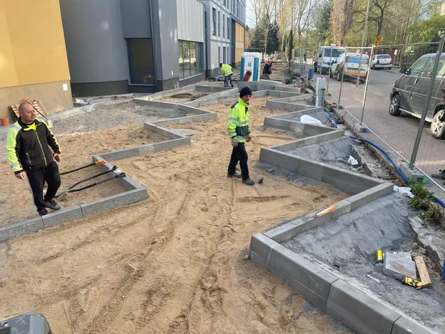 Dwóch pracowników montuje krawężniki w wykopie obok zgromadzonych materiałów