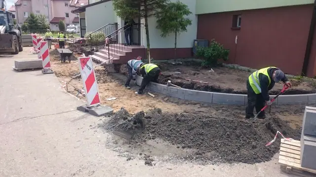 Ekipa w kamizelkach odblaskowych formuje nowe obrzeże trawnika zaprawą betonową przy wejściu
