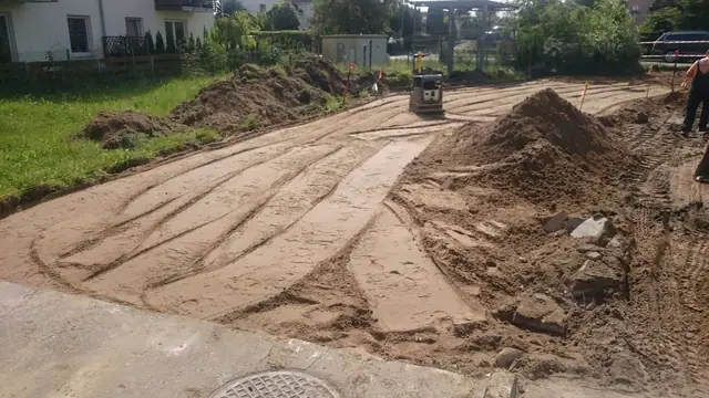 Rozjeżdżony piaszczysty plac przygotowywany pod nawierzchnię, widoczny właz kanalizacyjny