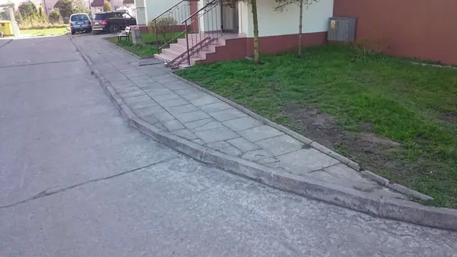 Stara popękana asfaltowa droga z krawężnikiem przed przebudową przy budynkach w Zieleniewie