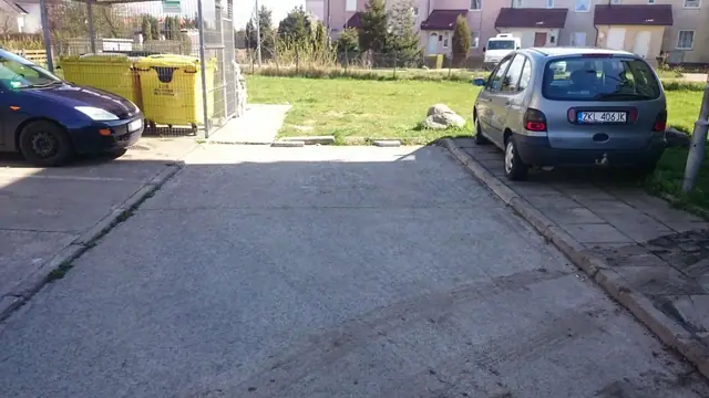Stary zniszczony wjazd asfaltowy pomiędzy zaparkowanymi samochodami przed remontem