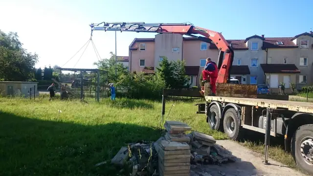 Żuraw ciężarówki rozładowuje elementy prefabrykowane na trawniku obok placu zabaw