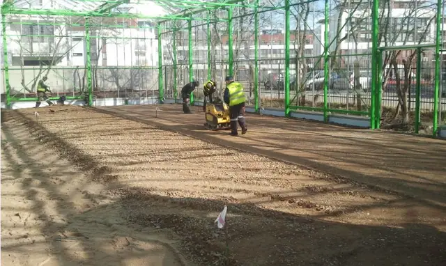Przygotowane podłoże żwirowe wewnątrz stalowej konstrukcji nowej hali, robotnicy zagęszczają teren