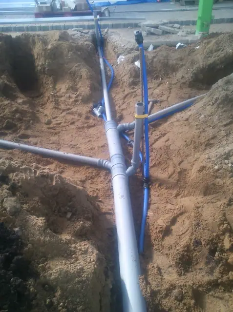 Węzeł niebieskich rur instalacji wodociągowej połączonych w piaszczystym wykopie