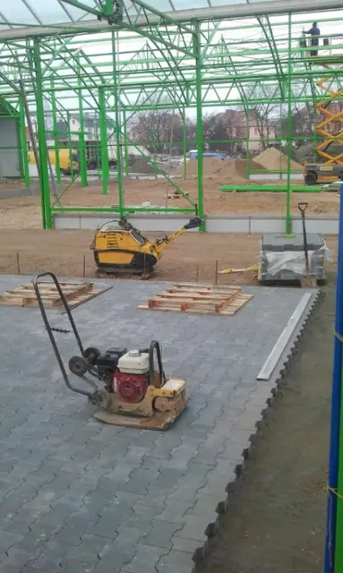 Zagęszczarka płytowa na ułożonej kostce brukowej przy stalowej konstrukcji nowej hali