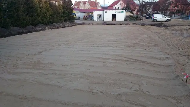 Wyrównany piaszczysty teren ze śladami zagęszczarki przygotowany pod kostkę parkingową
