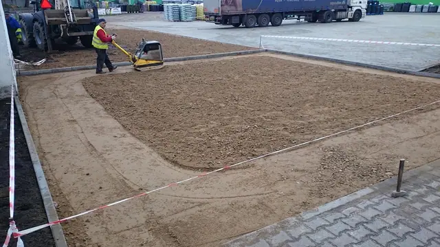 Pracownik zagęszcza piasek zagęszczarką przy krawędzi ułożonej kostki